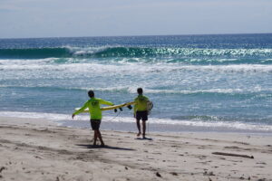 Surfers walk toward the ocean as a perfect turquoise blue wave breaks in Costa Rica