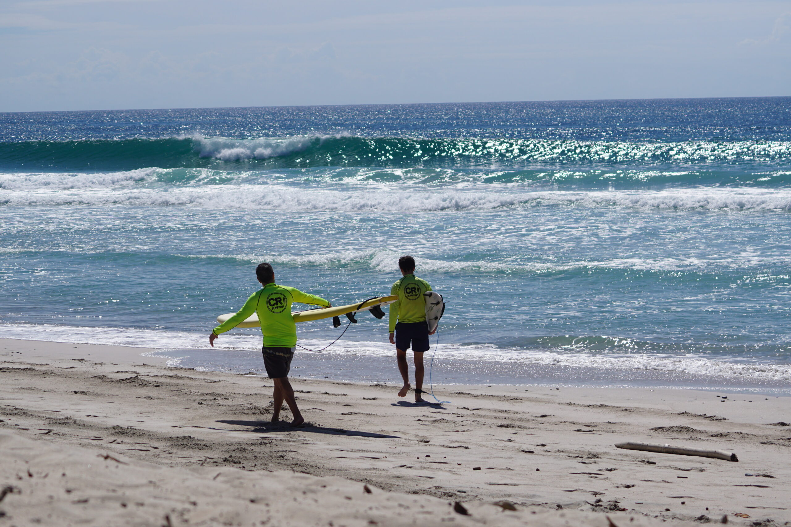 Surf Coaching Session Costa Rica Surfers walk toward the ocean as a perfect turquoise blue wave breaks in Costa Rica