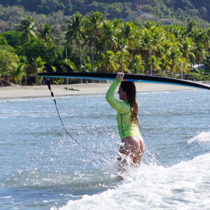 Costa Rica Surf camp surfer girl with her board in the tropical water in front of a palm tree lined beach