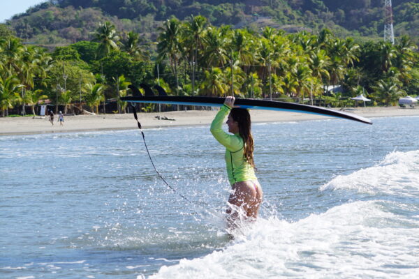 Costa Rica Surf camp surfer girl with her board in the tropical water in front of a palm tree lined beach