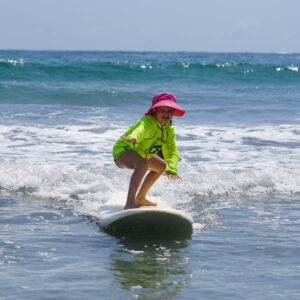 Little girl smiles as she surfs directly toward the camera in Costa Rica during her surf lesson