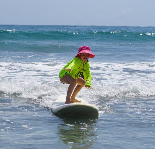 Little girl smiles as she surfs directly toward the camera in Costa Rica during her surf lesson