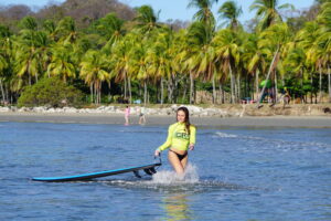 Surfer girl walks in the water in tropical paradise in Costa Rica with Costa Rica Surf Trip! at her Samara Surf Camp